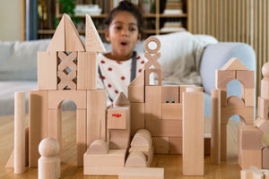Girl making an excited face sitting on a couch building a castle out of HABA wooden blocks