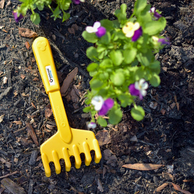 Yellow hand rake from the Spielstabil 2 Piece Garden Set in the garden with purple flowers