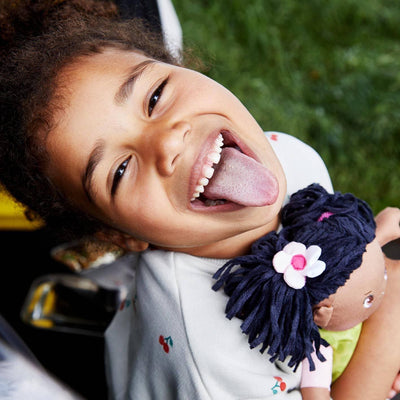 Girl looking at the camera sticking out her tongue holding Cari 12" Soft Doll - HABA USA
